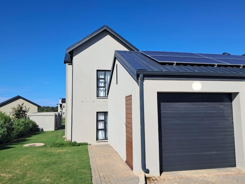 Modern apartment exterior featuring a garage with integrated solar panels, a paved walkway, and well-maintained surrounding lawn.
