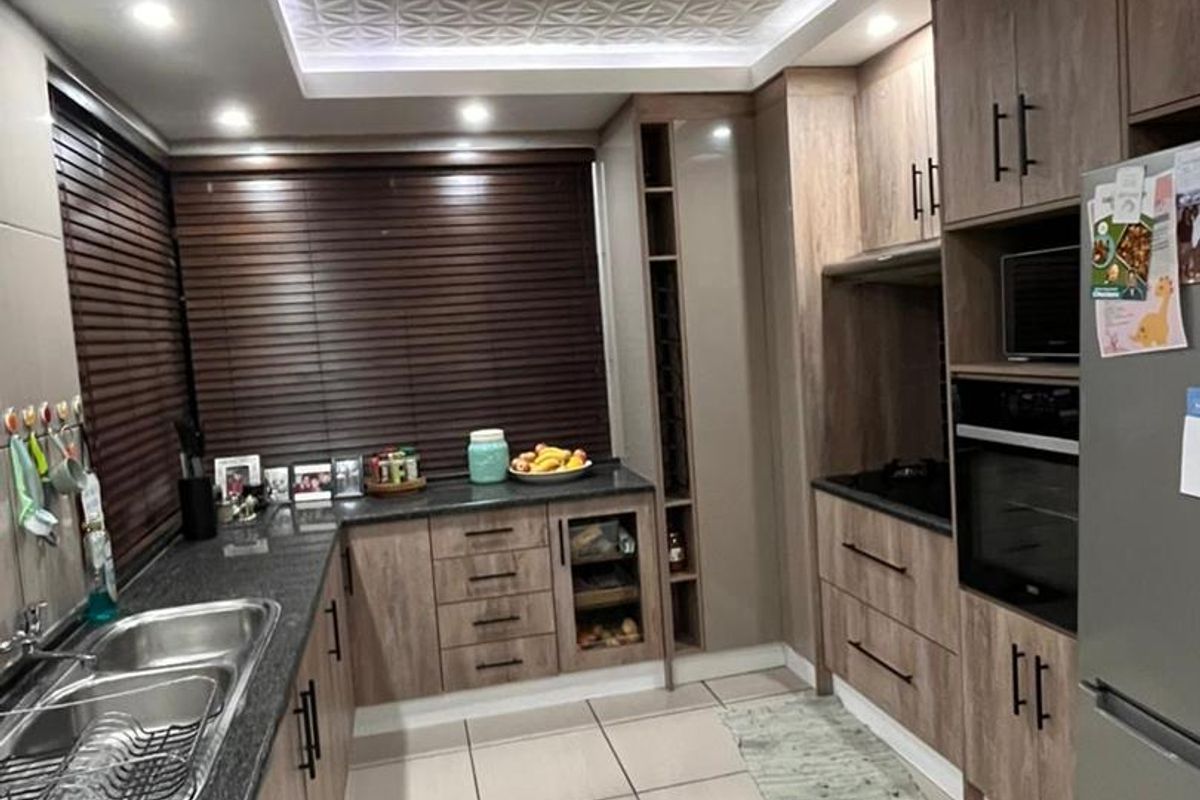 Modern kitchen featuring wood-grain cabinetry, granite countertops, double stainless steel sink, built-in oven, and a decorative coffered ceiling with recessed lighting.
