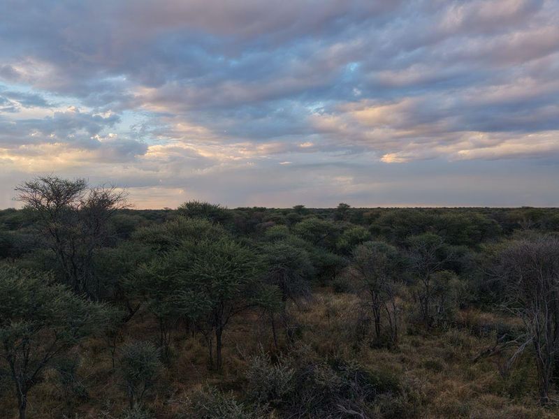 Expansive scenic view of the natural bushveld landscape under a dramatic cloudy sky, showcasing the property's rural setting.