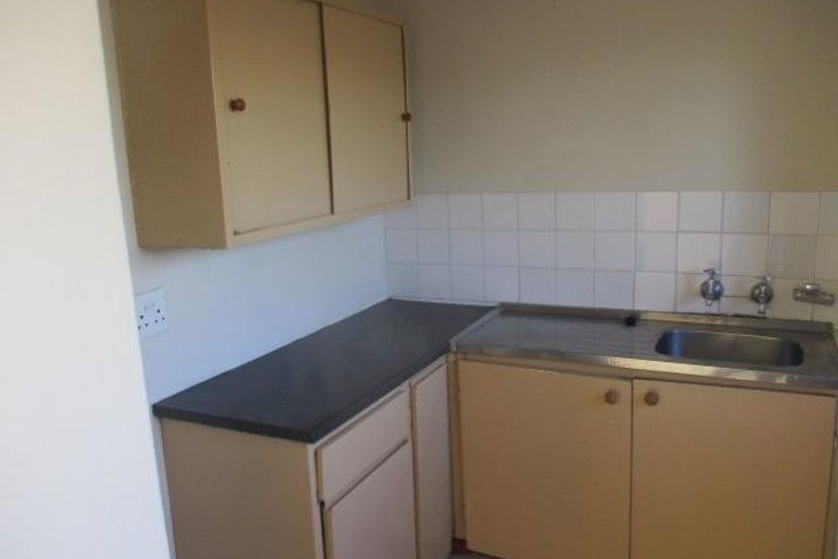 A compact kitchen area featuring dated laminate cabinetry, a stainless steel sink, and a tiled splashback, offering potential for a modern renovation.