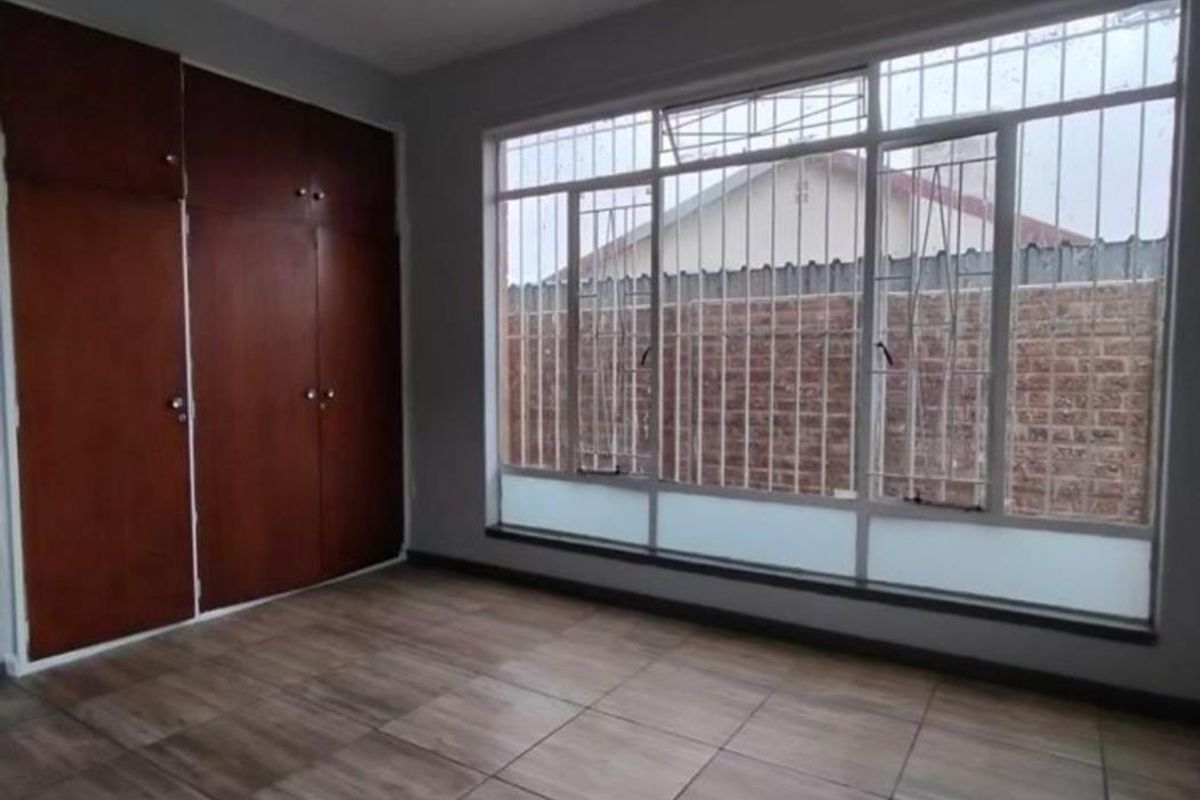 A vacant bedroom featuring wood-look tiled flooring, large windows with security bars, and built-in wooden cupboards.