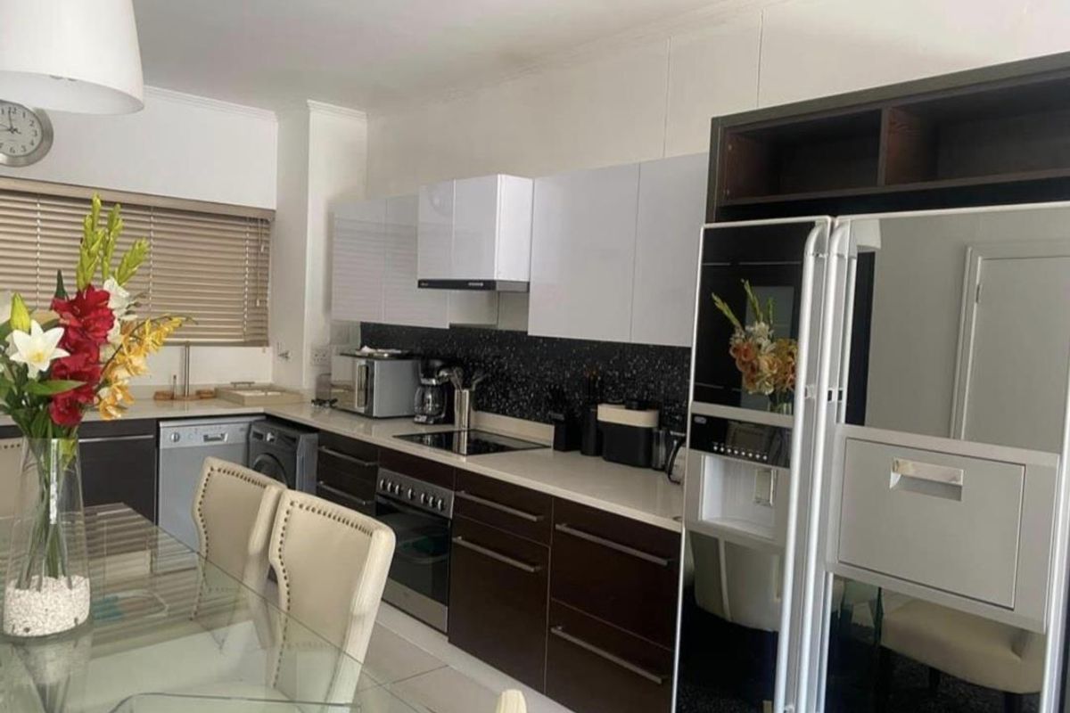 Modern kitchen featuring dark lower cabinetry, white upper cabinets, stone countertops, integrated appliances, and a sleek black tiled backsplash.