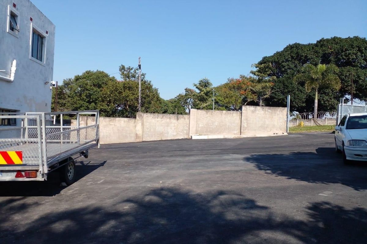 Rear exterior area featuring paved parking space, perimeter boundary wall, and security fencing.