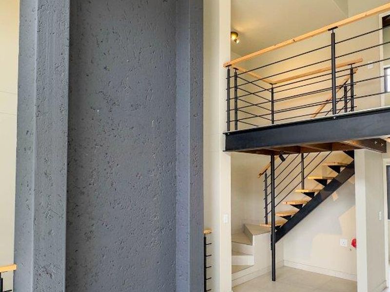 Spacious living area featuring a double-volume ceiling with exposed timber trusses, a striking textured feature wall, and a modern staircase leading to a mezzanine level.
