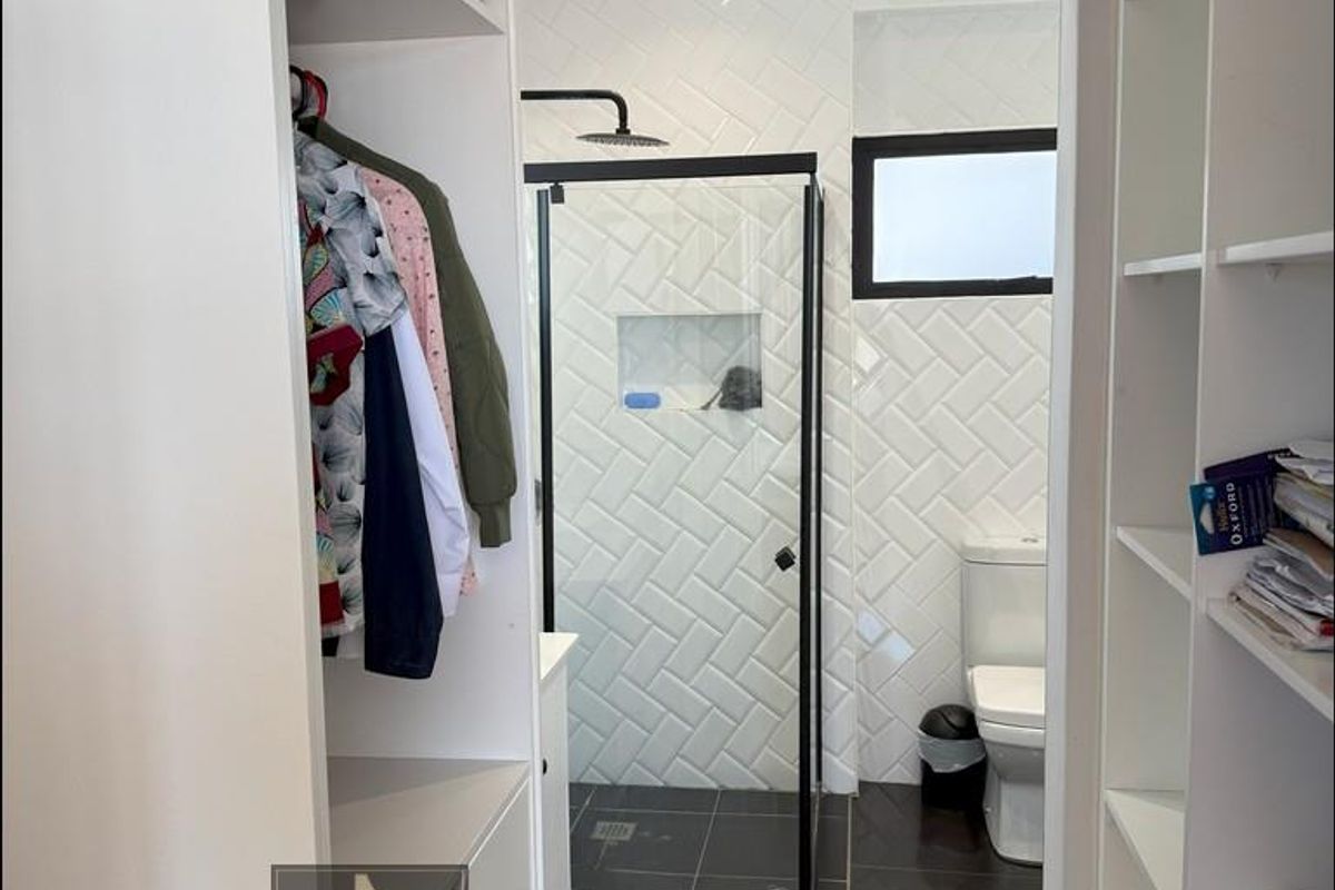 A modern bathroom featuring a walk-in shower with black frame, herringbone wall tiling, and an adjacent walk-in closet with built-in shelving.
