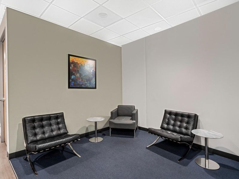 A professional office waiting area featuring a suspended ceiling, recessed lighting, and dark blue carpeting, creating a clean and functional workspace environment.