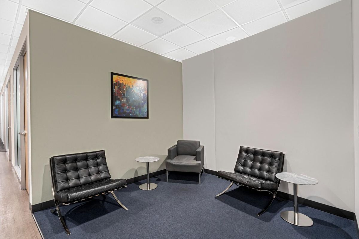 A professional office waiting area featuring a suspended ceiling, recessed lighting, and dark blue carpeting, creating a clean and functional workspace environment.