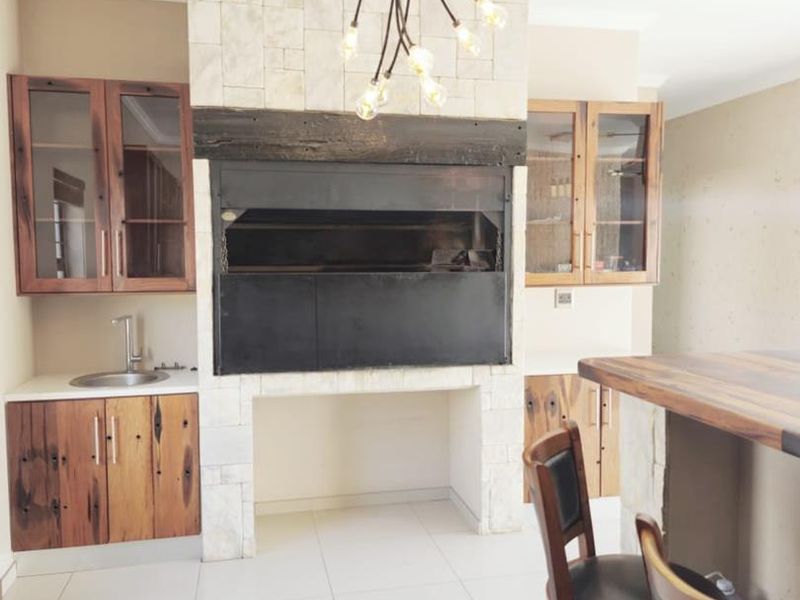 A well-appointed indoor bar area featuring a built-in braai with stone cladding, custom timber cabinetry, and a breakfast bar counter.