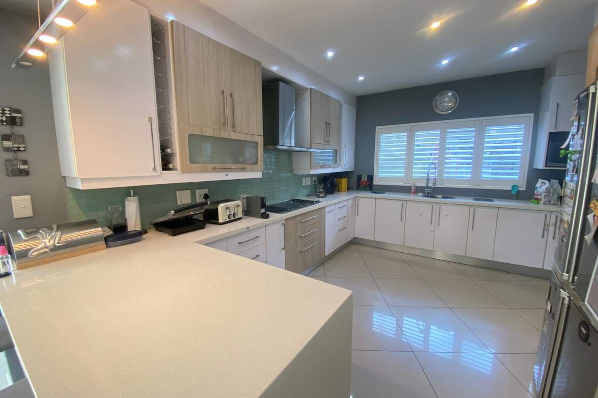 Modern kitchen featuring stone countertops, two-tone cabinetry, integrated hob and extractor fan, tiled flooring, and plantation shutters.