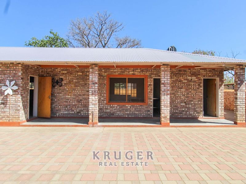 A rear view of a house featuring an exposed brick facade, a covered patio area, and a paved driveway.