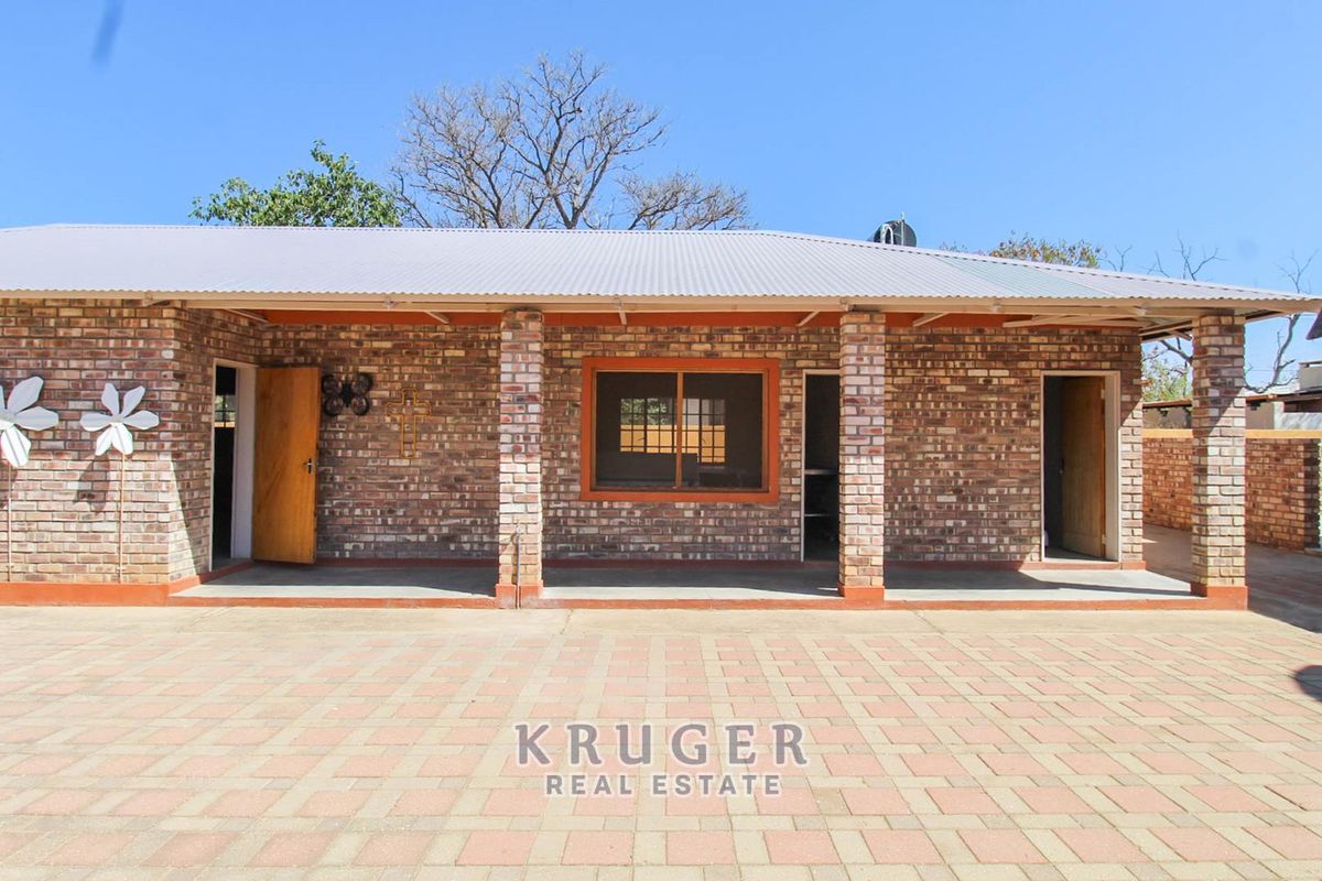 A rear view of a house featuring an exposed brick facade, a covered patio area, and a paved driveway.