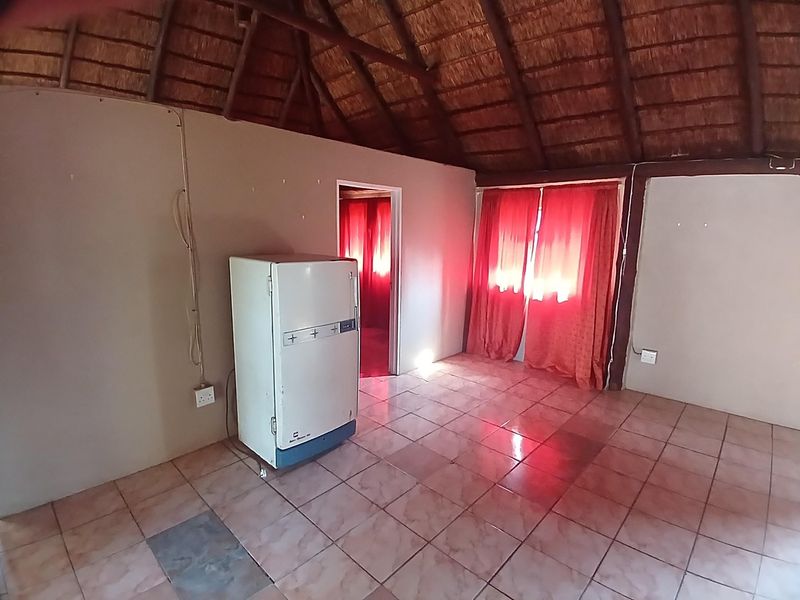 An empty living area featuring a traditional thatched roof with exposed timber beams and ceramic tiled flooring.