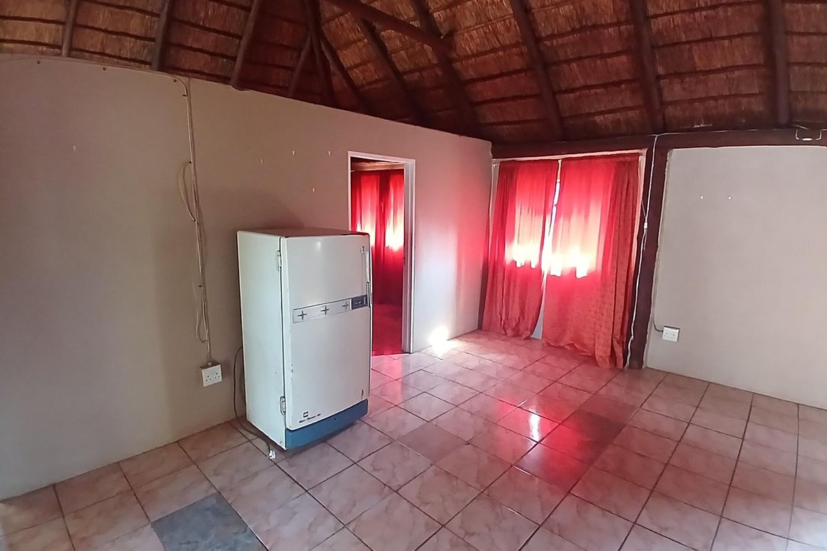 An empty living area featuring a traditional thatched roof with exposed timber beams and ceramic tiled flooring.