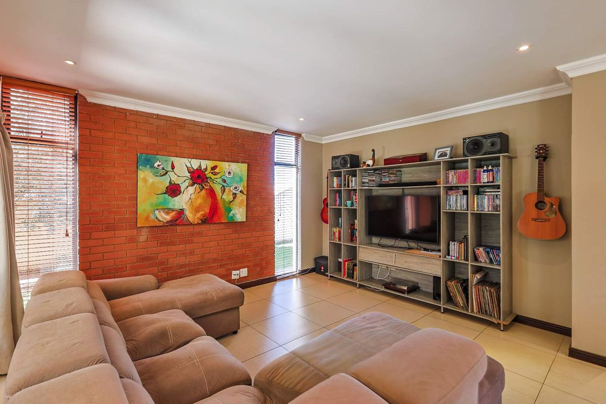A comfortable living room featuring a distinctive exposed red brick feature wall, tiled flooring, and recessed downlighting.