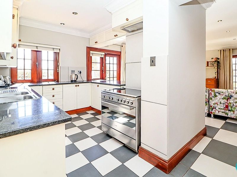 A well-maintained kitchen featuring granite countertops, a stainless steel freestanding stove, and classic checkered floor tiles, offering a functional and bright cooking space.