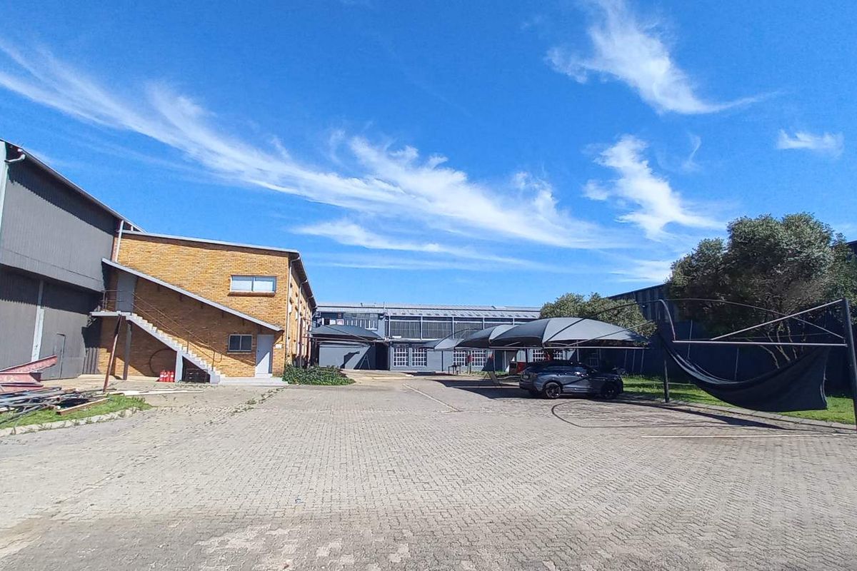 Spacious industrial yard featuring paved driveway, external staircase access, and multiple shade cloth carports between large metal-clad warehouse structures.
