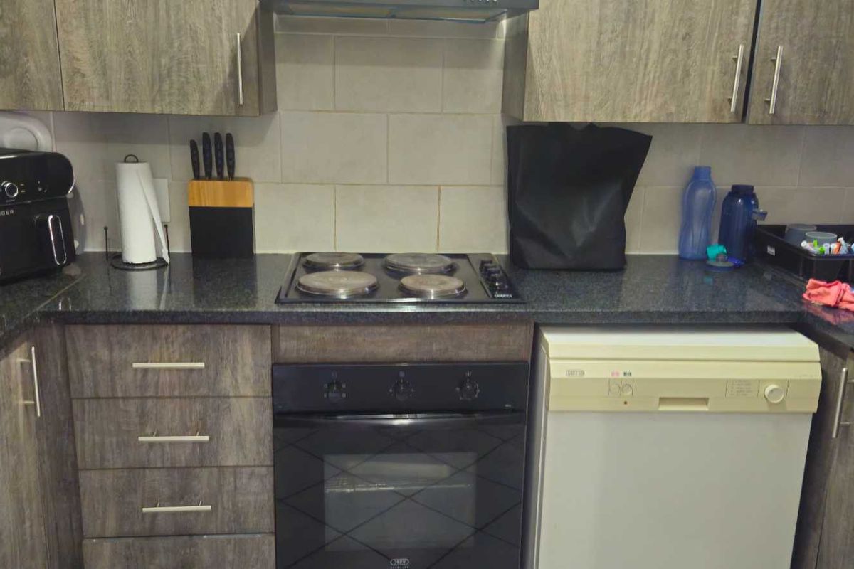 A functional kitchen featuring wood-look laminate cabinetry, granite countertops, a built-in oven with electric hob, and a tiled backsplash.