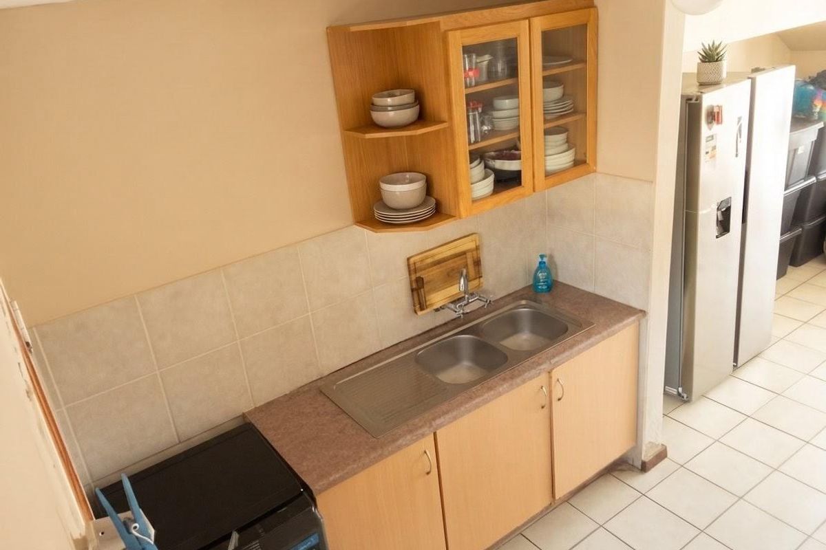 A functional kitchen area featuring laminate countertops, a double bowl stainless steel sink, tiled splashbacks, and ample wooden cabinetry for storage.