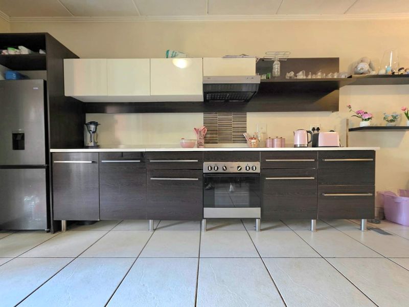 A modern kitchen featuring dark wood-grain cabinetry, white upper cabinets, a built-in oven with extractor fan, and light-colored tiled flooring.