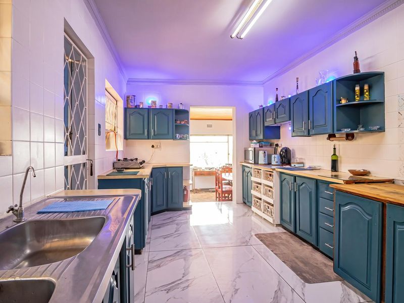 A functional kitchen featuring blue cabinetry, wooden countertops, tiled flooring, and a double stainless steel sink with direct access to an adjacent room.