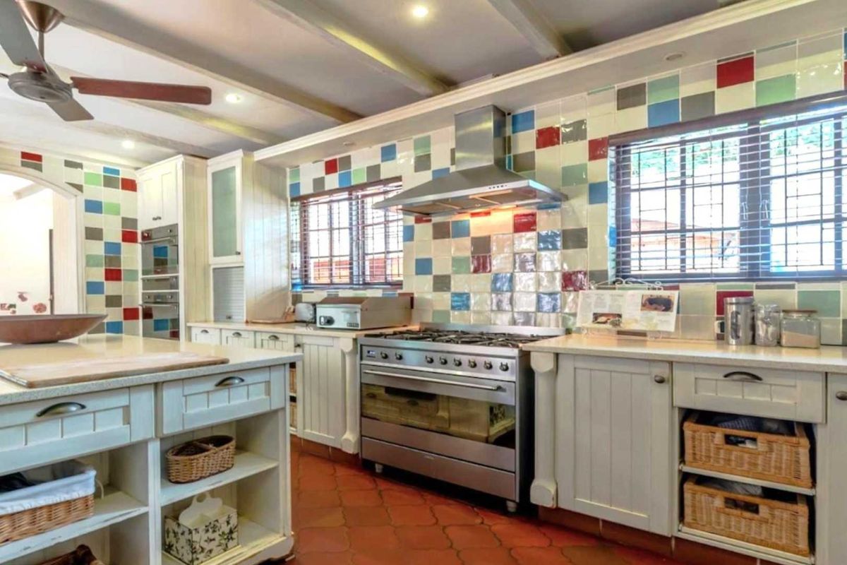 A spacious kitchen featuring a large central island, stainless steel gas range with extractor hood, and ample cabinetry with a distinctive multi-colored tile splashback.
