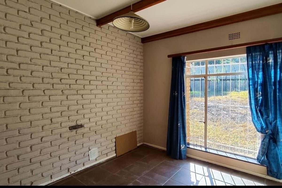 A bedroom featuring a distinctive painted brick feature wall, tiled flooring, and a large window with security bars overlooking the garden.