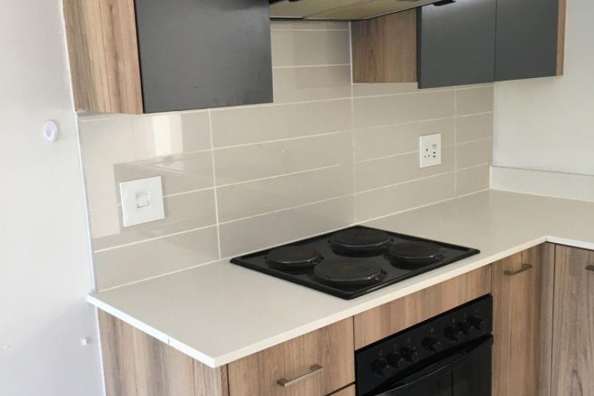 Modern kitchen featuring wood-grain cabinetry, stone-look countertops, a built-in oven, electric hob, and a sleek extractor fan with tiled splashback.