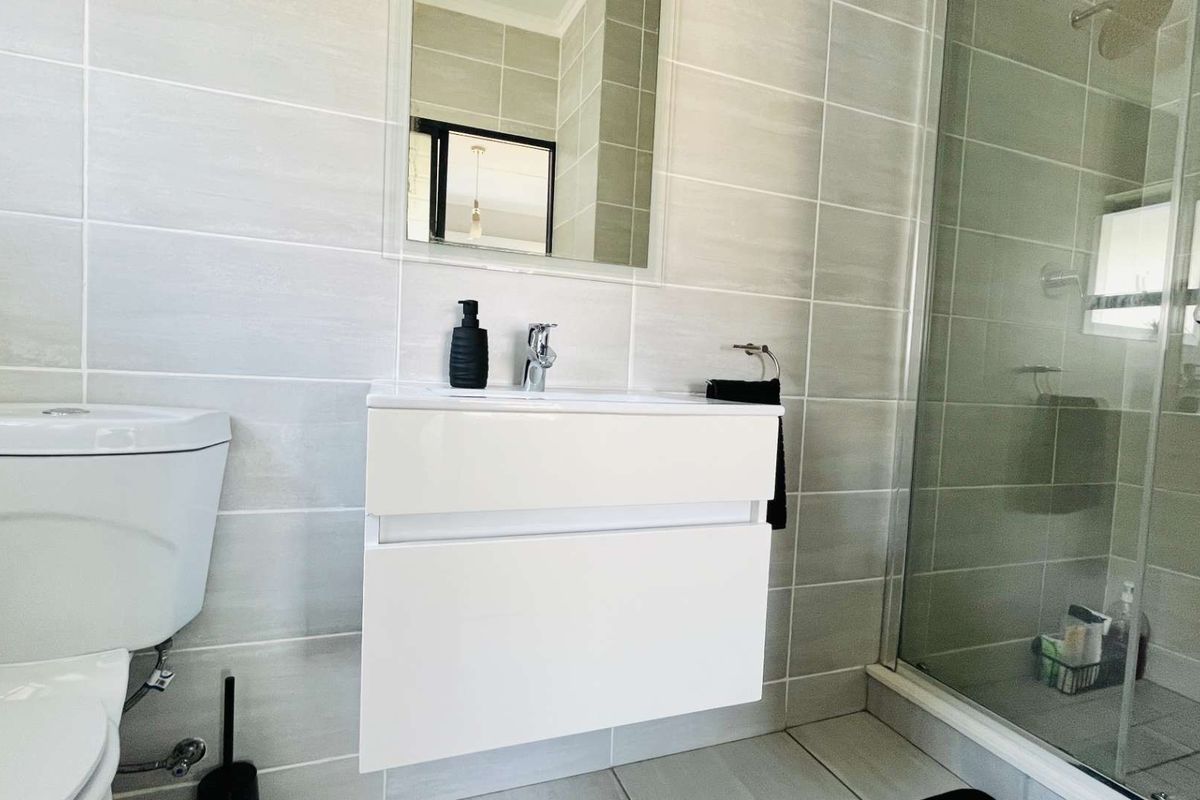 Modern bathroom featuring a wall-mounted vanity, glass shower enclosure, and neutral ceramic tiling throughout.