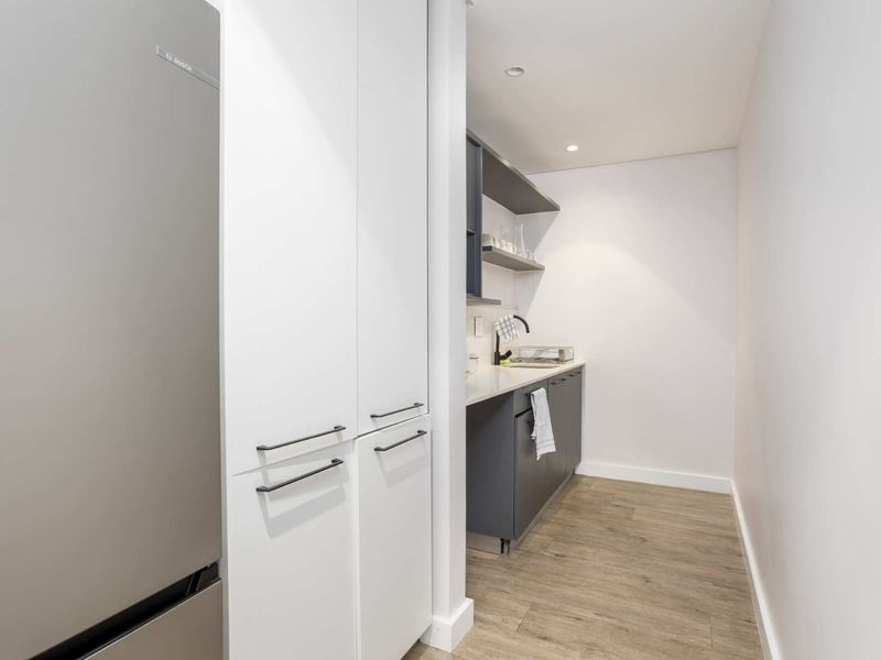 A modern, well-maintained scullery featuring sleek white and grey cabinetry, open shelving, and a functional sink area with wood-look flooring.