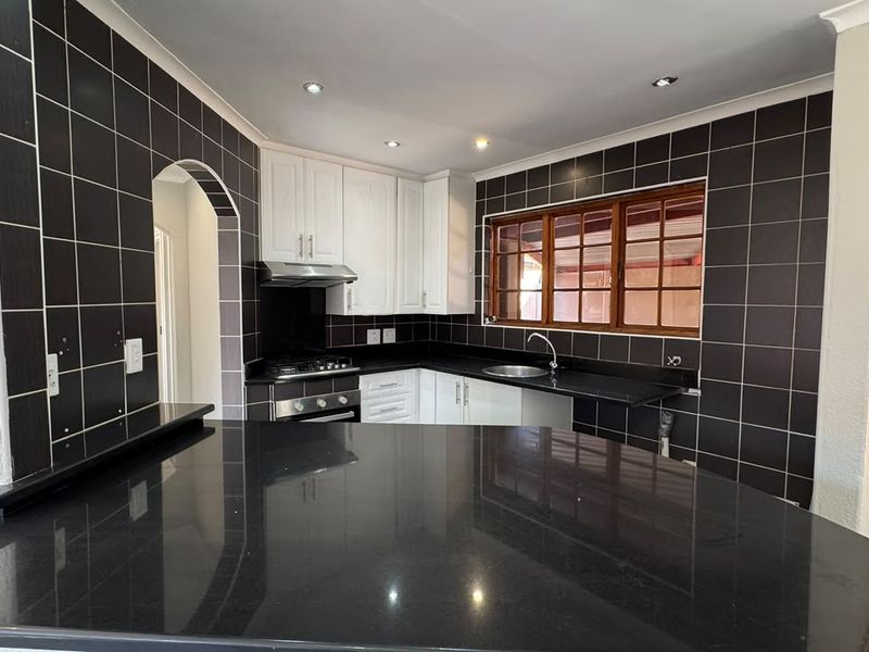 A clean, modern kitchen featuring white cabinetry, contrasting black granite countertops, dark tiled walls, and a built-in gas hob with an extractor fan.