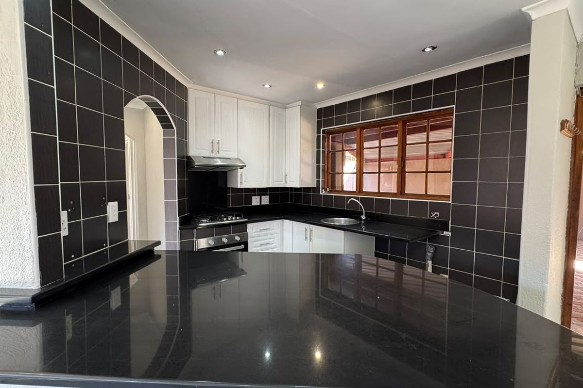 A clean, modern kitchen featuring white cabinetry, contrasting black granite countertops, dark tiled walls, and a built-in gas hob with an extractor fan.