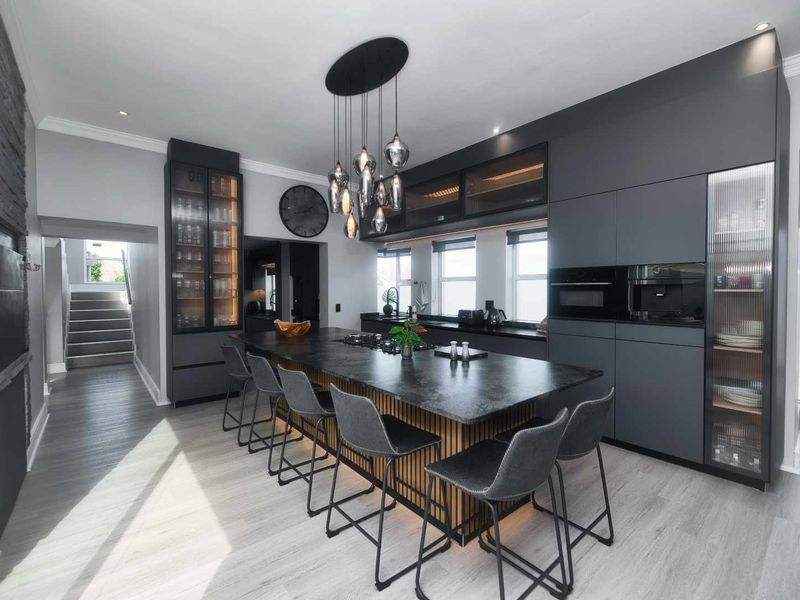 Modern, high-end kitchen featuring a large central island with stone countertops, integrated appliances, sleek dark cabinetry, and stylish pendant lighting.