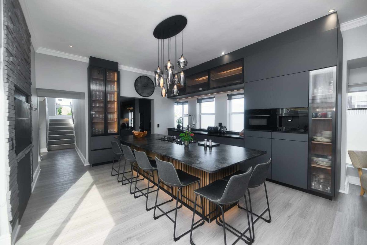 Modern, high-end kitchen featuring a large central island with stone countertops, integrated appliances, sleek dark cabinetry, and stylish pendant lighting.