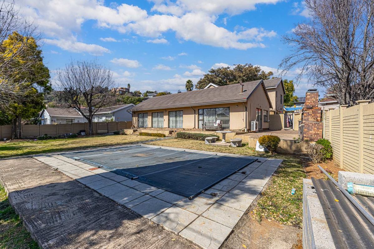 Rear view of the property featuring a swimming pool with cover, paved patio area, and an outdoor brick fireplace set within a private garden.