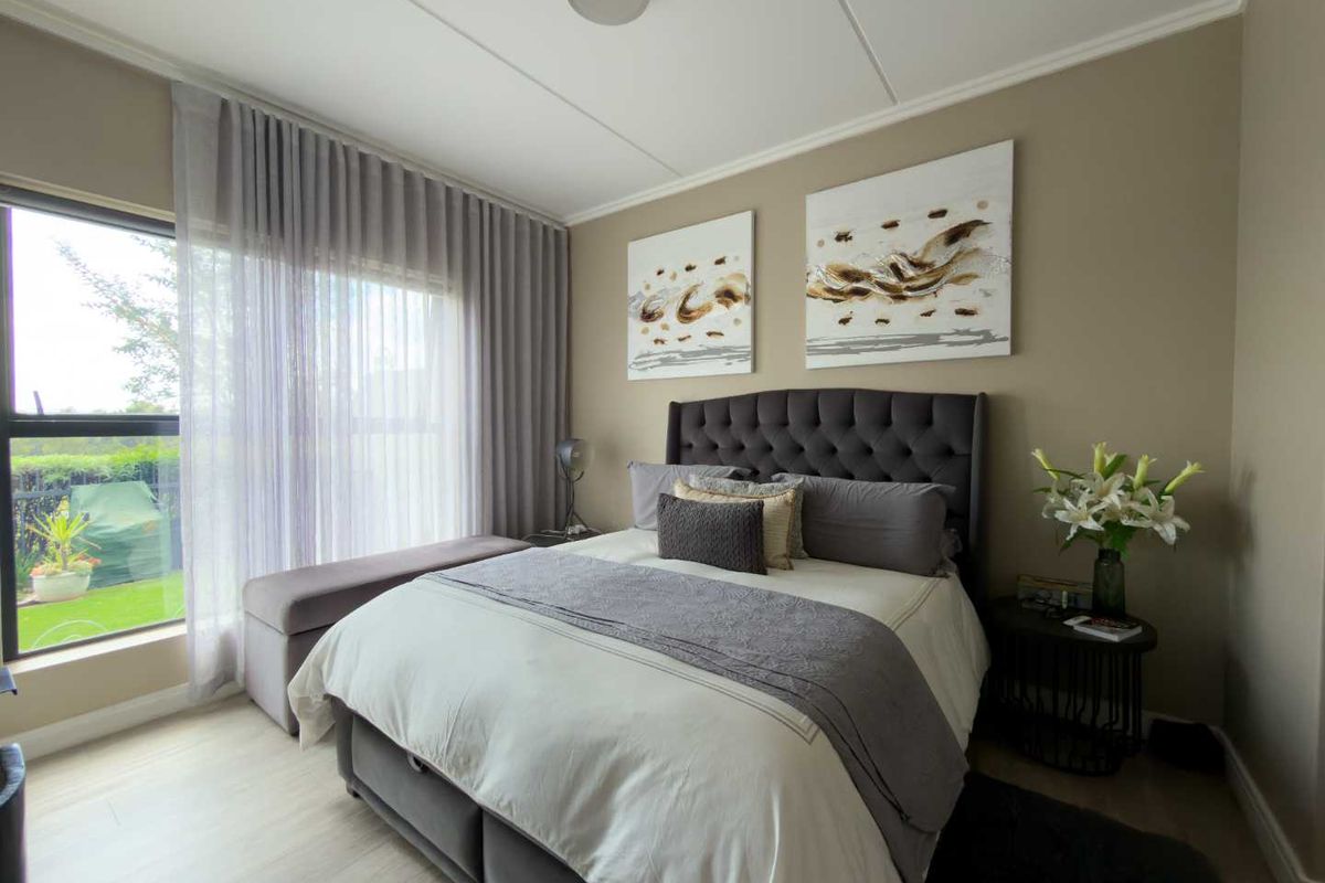 A well-maintained bedroom featuring light-toned flooring, neutral wall finishes, and a large window with floor-to-ceiling curtains providing natural light.