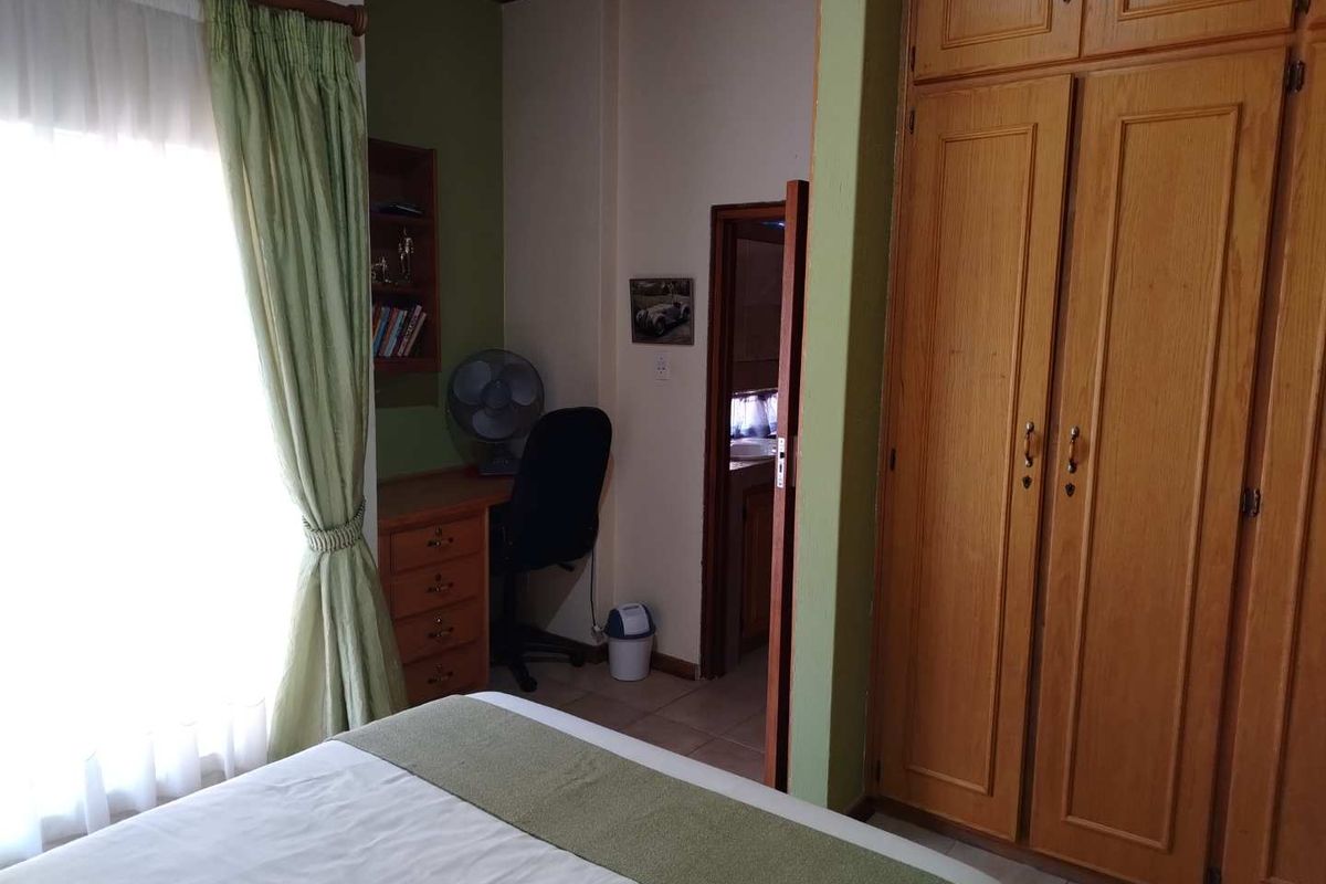 Bedroom featuring built-in wooden cupboards, a dedicated study nook with shelving, and an adjoining doorway leading to an en-suite bathroom.