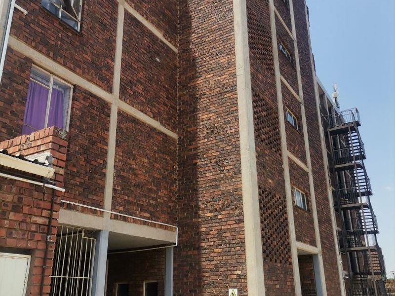 Exterior view of a multi-story apartment building featuring exposed brickwork, concrete structural framing, and an external metal fire escape staircase.