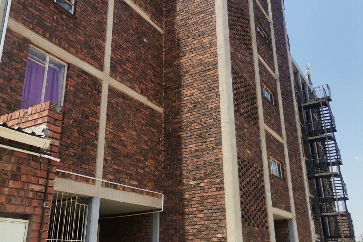 Exterior view of a multi-story apartment building featuring exposed brickwork, concrete structural framing, and an external metal fire escape staircase.