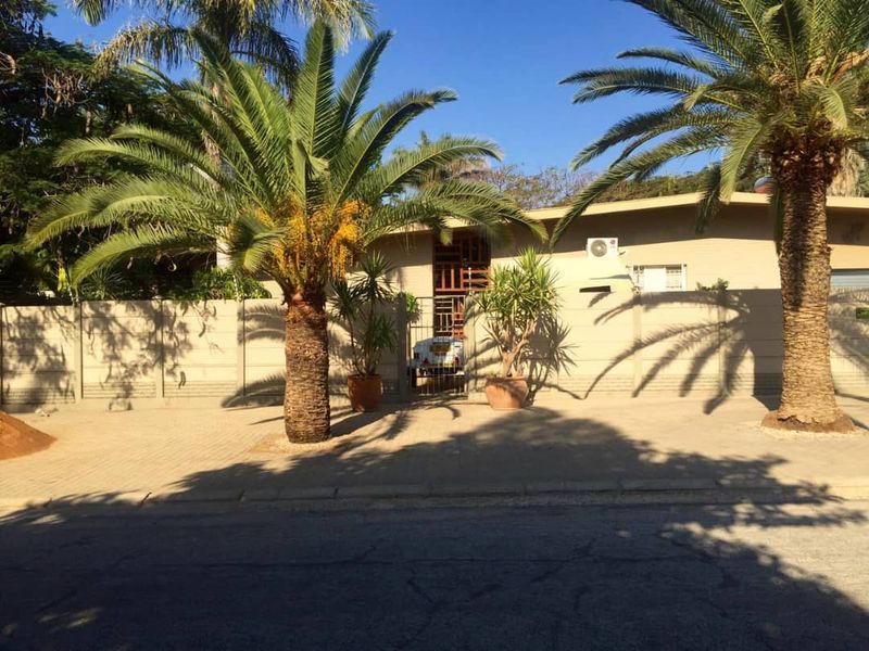 Front exterior view of the property featuring a paved driveway, perimeter wall, and mature palm trees.
