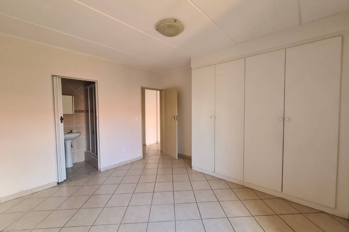 A spacious, empty bedroom featuring neutral tiled flooring, ample built-in cupboard storage, and direct access to an en-suite bathroom.