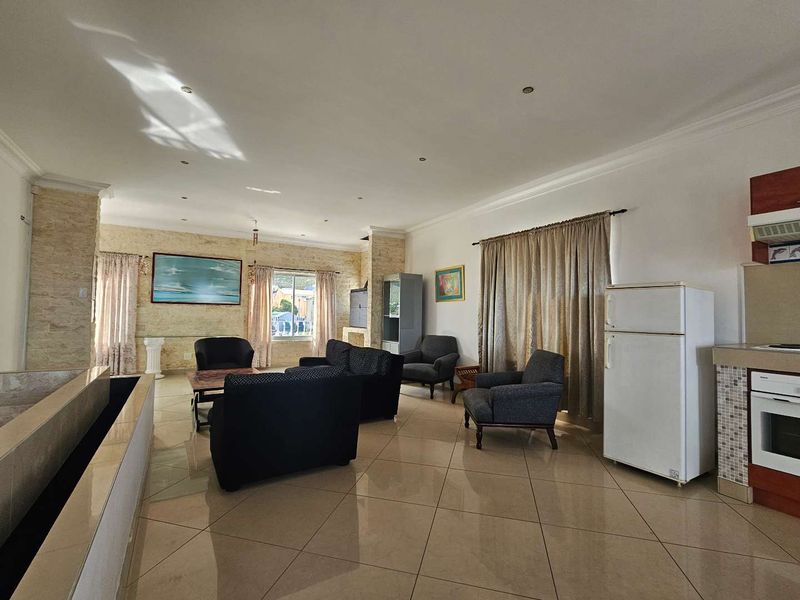 Spacious open-plan living area featuring tiled floors, a stone accent wall, and a functional kitchen with built-in oven and hob.