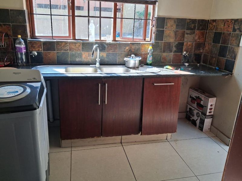 Functional laundry area featuring a double basin sink, granite countertops, built-in cabinetry, and tiled splashback with natural light from the window.