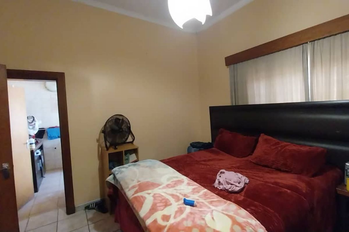 A bedroom featuring tiled flooring, a built-in doorway leading to an adjacent space, and a large window with wooden trim.