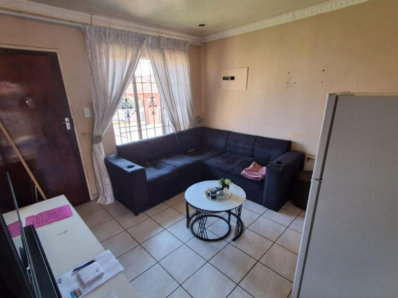 A compact living area featuring tiled flooring, decorative ceiling cornices, and a window fitted with security bars.