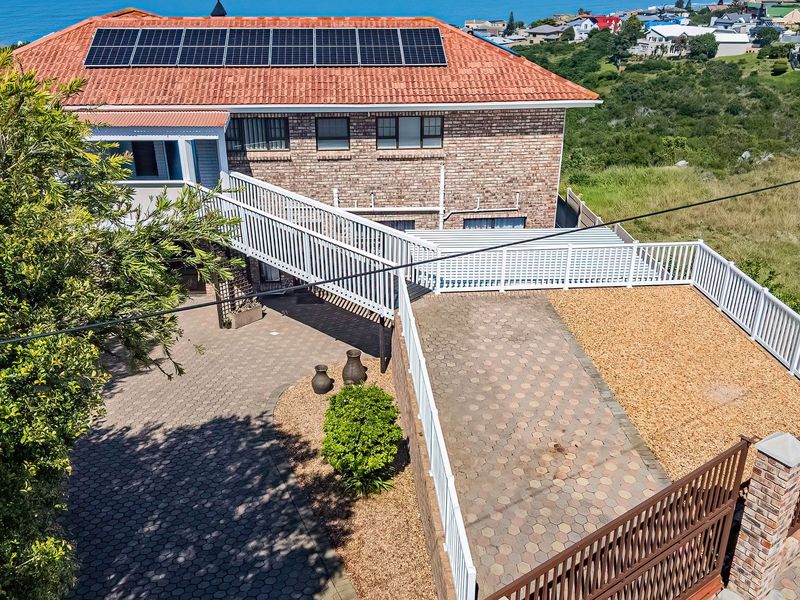 Aerial view of a brick house featuring a tiled roof with solar panels, a raised walkway, paved driveway, and secure perimeter fencing.