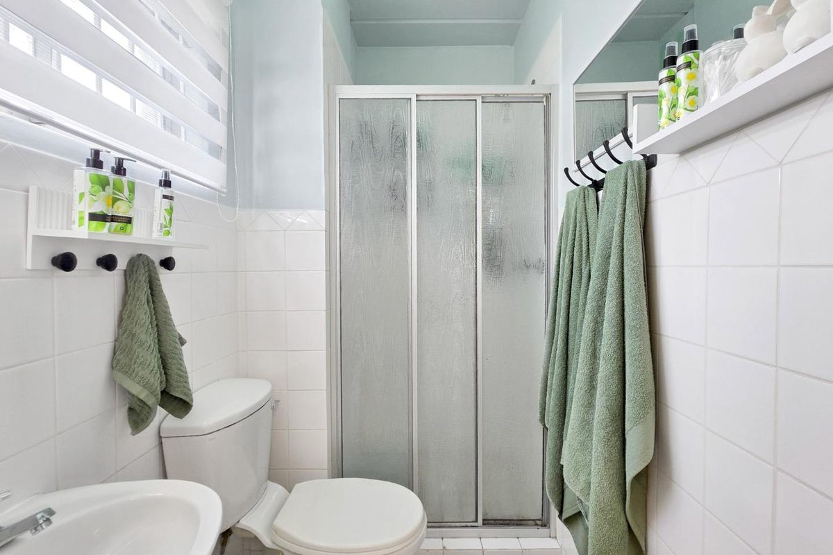 A functional bathroom featuring a shower enclosure with sliding doors, a pedestal basin, a toilet, and white wall tiling.