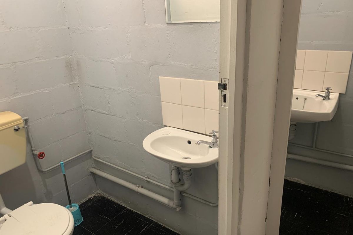 A functional office bathroom featuring basic sanitary ware, exposed plumbing, and painted blockwork walls.