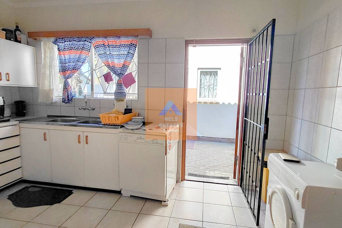 Functional kitchen featuring built-in cabinetry, tiled splashbacks, and direct access to an outdoor paved area through a security gate.