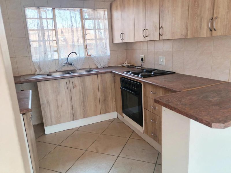 A functional kitchen featuring light wood-look cabinetry, laminate countertops, a built-in oven with electric hob, and tiled flooring throughout.