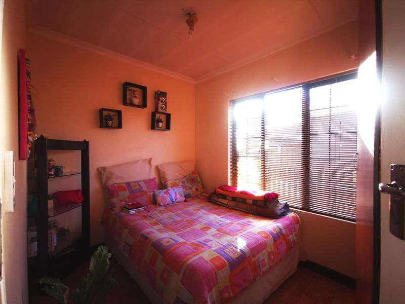 A compact bedroom featuring laminate flooring and venetian blinds, providing natural light and a functional layout.